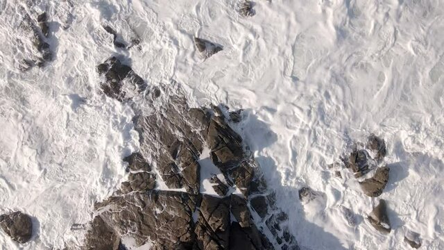 Plano a&eacute;reo zenital desde drone de mar picado con olas con mucho viento chocando contra rocas en la costa.