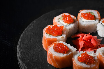 classic Philadelphia rolls in smoked salmon with salmon caviar. japanese sushi on a slate board on a dark background.
