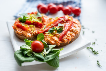 vegan roasted red pepper dip sandwich spread on freshly baked bread slice with salad garnish on white porcelain plate 