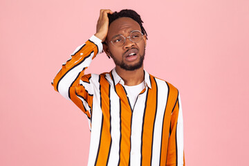 Bewildered perplexed afro-american man with dreadlocks in striped stylish shirt scratching his...
