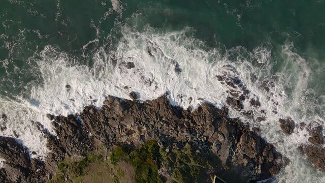 Plano a&eacute;reo zenital desde drone de mar picado con olas con mucho viento chocando contra rocas en la costa.