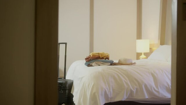 dolly shot of Travelers necessity. unpacked travelers suitcase is standing beside the bed with stack of casual cloth on bed in hotel room holiday vacation travel concept
