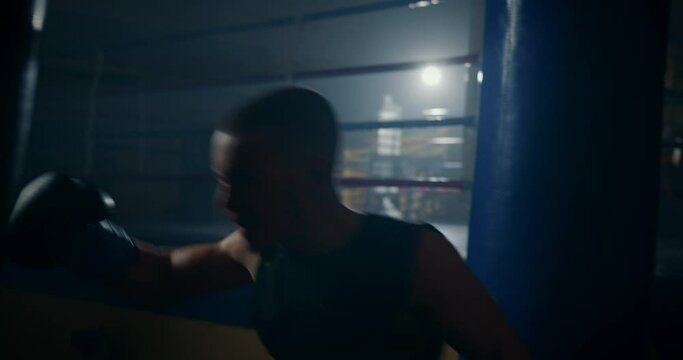 Dynamic shot of young persistent male athlete punching bag training hands muscles. Boxer getting ready for kickboxing competition.