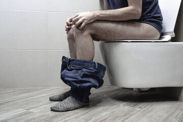 Closeup view of man suffering from hemorrhoid on toilet bowl in rest room