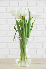 White tulips in glass vase on background white brick wall