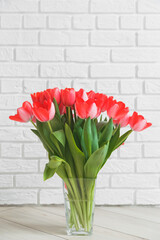 Pink tulips in glass vase on background white brick wall.