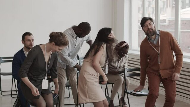 Medium long of diverse multiethnic business people in conference room standing up, putting notebooks and things on chairs, clapping hands and smiling