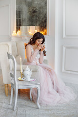 Morning of the bride. She is in a white interior drinking tea. The room has a classic white fireplace