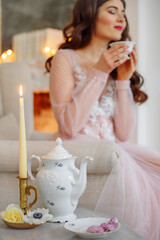 Morning of the bride. She is in a white interior, drinking tea, a candle is burning on the table