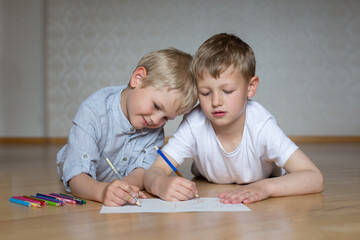 two boys are drawing with colored pencils while lying on the floor. School children do their homework