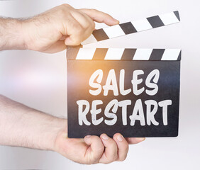 Obraz premium On a white background, a man holds a clapperboard in his hands on which it is written - SALES RESTART