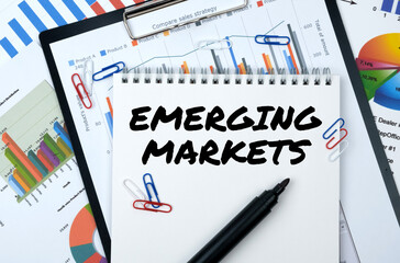 On the table are reports, charts, a notebook with the inscription - EMERGING MARKET