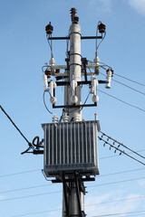 High voltage transformer mounted on a pole on blue sky background at sunny day. Vertical orientation