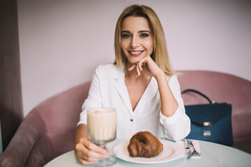 Smiling lady sitting in cafeteria with croissant and milkshake