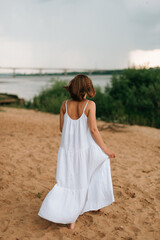 a girl in a white dress walks along the sandy shore