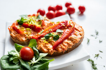 vegan roasted red pepper dip sandwich spread on freshly baked bread slice with salad garnish on white porcelain plate 
