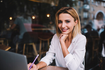 Smiling female freelancer working on laptop on terrace and looking at camera