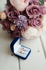 wedding bouquet and wedding rings lie on a white wooden table