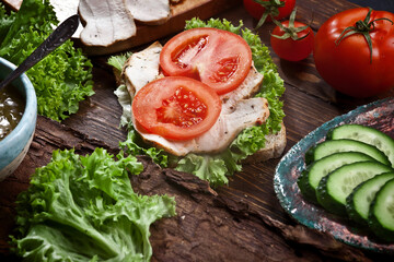 turkey meat sandwich with tomatoes, green salad and cucumbers on dark wooden table background