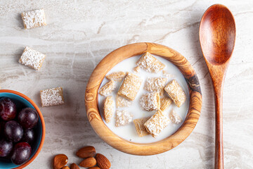 A simple breakfast concept with a bowl of frosted bite size wheat cereal in milk on marble kitchen countertop. There are grapes and nuts as appetizers. A healty snack with vitamins and fiber.