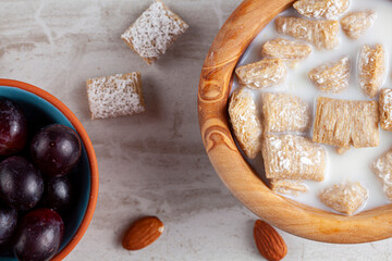A simple breakfast concept with a bowl of frosted bite size wheat cereal in milk on marble kitchen countertop. There are grapes and nuts as appetizers. A healty snack with vitamins and fiber.