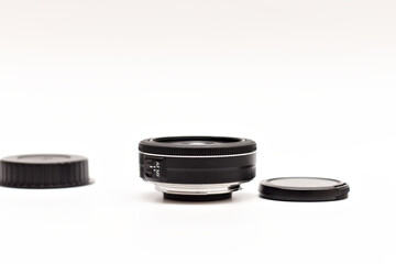 A small black 24mm lens with no name for a digital SLR camera lying on a white background. The covers are lying side by side