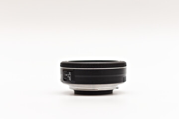 A small black 24mm lens with no name for a DSLR camera lying on a white background without caps. Side view