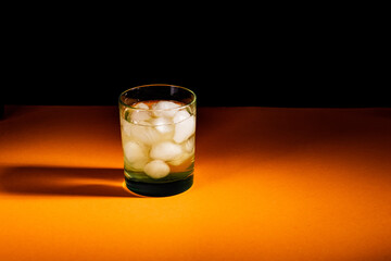 a glass with ice and absinthe stands on an orange table in a dark room