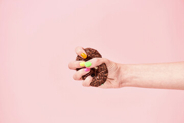 Say no to unhealthy eating. Female hand squeezing chocolate donut on pink background