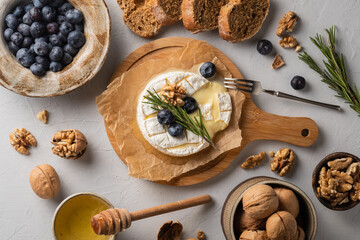 Camembert cheese on paper, blueberrys, nuts. honey, sandwicheson on grey background. Italian, French cheese.