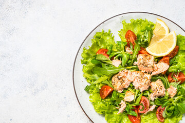 Fresh Salad with green leaves and baked salmon. Top view at white table.