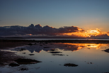 Landscape with sunset over calm ocean, some dreamy purple, orange clouds and mirror like reflection in water