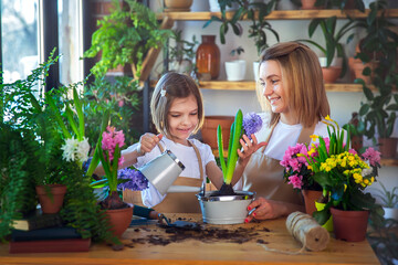 Cute child girl helps her mother to care for plants. Mom and her daughter engaged in gardening. Happy family in spring day.