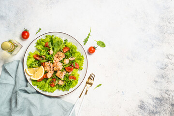 Salad with baked salmon fish. Green salad mix with tomatoes anf salmon. Top view at white table.