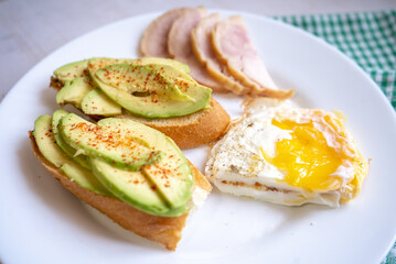 Home cooking breakfast with avocado toast, fried egg and ham on white plate