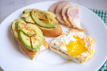 Home cooking breakfast with avocado toast, fried egg and ham on white plate
