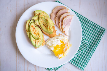 Home cooking breakfast with avocado toast, fried egg and ham on white plate