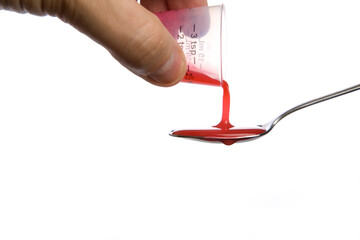 Hand pouring red medicine onto a metal spoon.