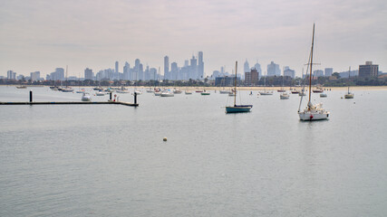 Yachts, sailboats and wooden dock on blue ocean water of Port Phillip Bay against a background of Melbourne skyline in a summer cloudy day, St. Kilda, Victoria, Australia