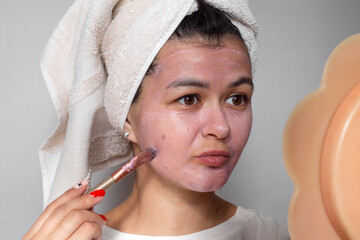 Face skin care at home concept. Happy young woman applying a pink mask on her face with a brush