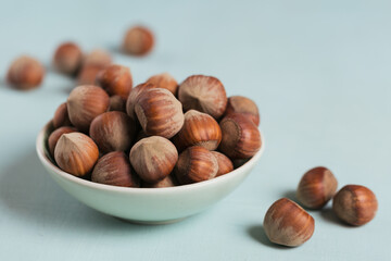 Pile of hazelnuts filbert in a bowl on a light blue background