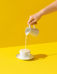 Pouring milk in a cup, on yellow background. Milk overflow from a cup