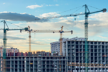 Construction site, cranes and multi-storey unfinished buildings at sunrise or sunset