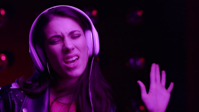 Close up portrait attractive brunette girl dancing Indoors with colourful purple neon light. club atmosphere. Overjoyed muslim young woman listening music and singing in headphones and dancing.