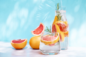 Summer cocktail with grapefruit and rosemary and juicy slices citrus fruits. Fresh healthy grapefruit beverage on sunlight with hard shadows. Creative drink with palm leaf on blue pastel background.