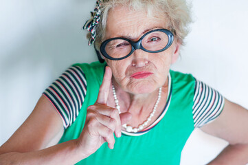 Stylish emotional elderly woman with an evil face waving index finger over white background....