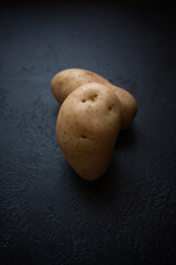 Funny potato in the face shape from home garden on a black textured  background.Trendy ugly organic...