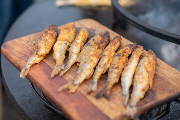 Crispy breaded european smelt fish on wooden cutting board at summer outdoor food market: close up. Seafood, barbecue, gastronomy, cookery, street food concept