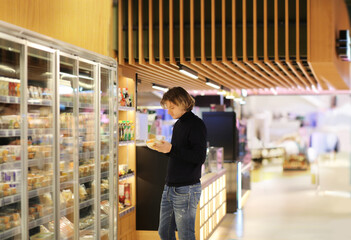 Young man shopping in supermarket, reading product information.