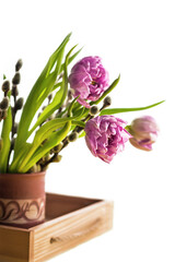 Bouquet of spring flowers in a vase on a wooden tray on a white background with copy space. Festive composition.